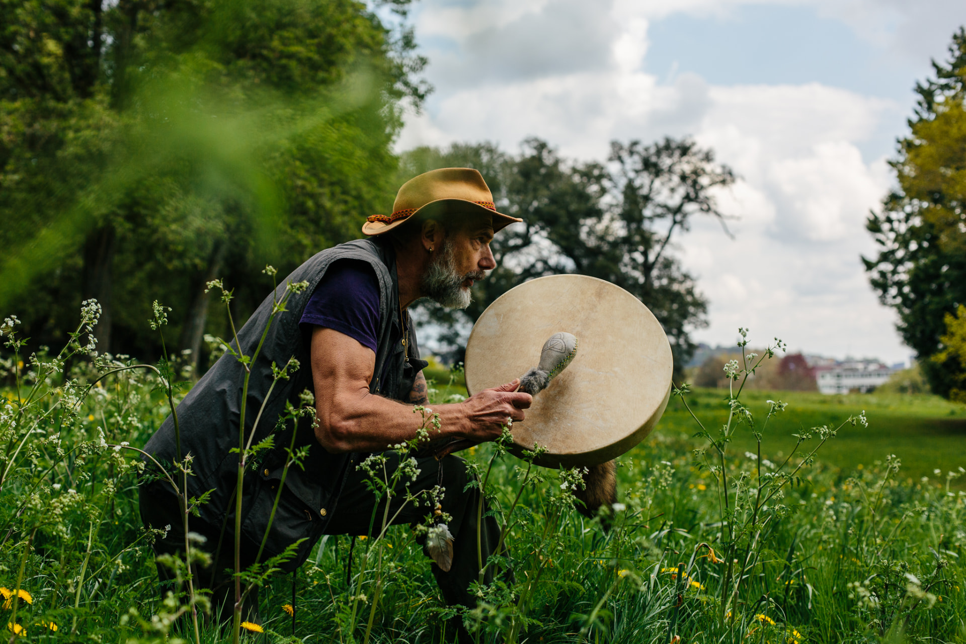 Christopher Gladwell playing a frame drum in a meadow of wildflowers