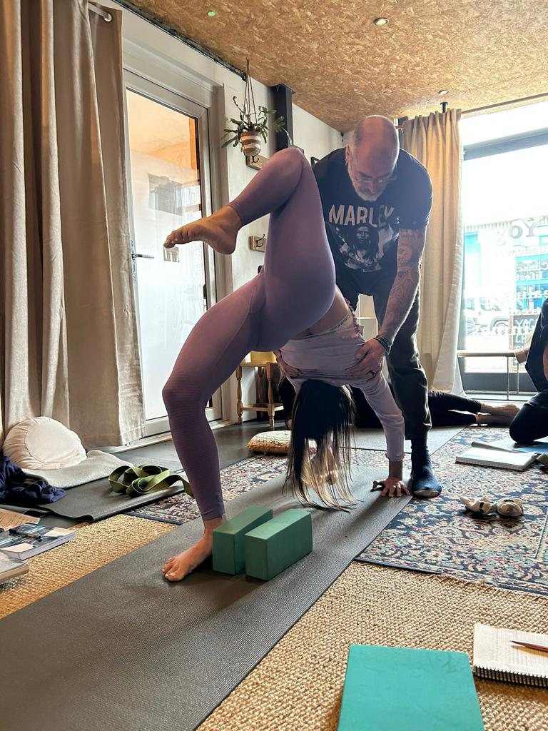 Christopher assisting a student in a backbend over yoga blocks